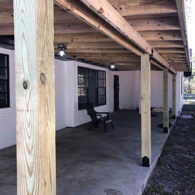 A wooden-covered patio with vertical support beams and two chairs rests on a concrete floor, creating a serene spot outside the white brick house in Lakeland.